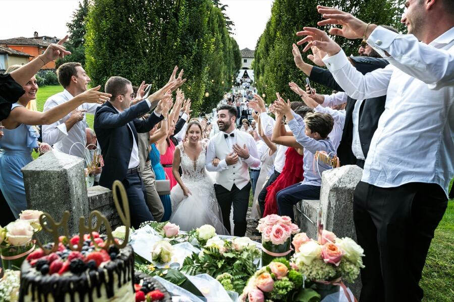 Bride and groom walking through guests reaching out to cheer them, with a cake in the foreground