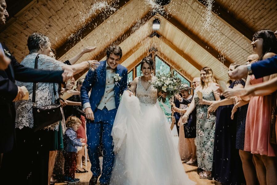 Couple walking under confetti with guests cheering them